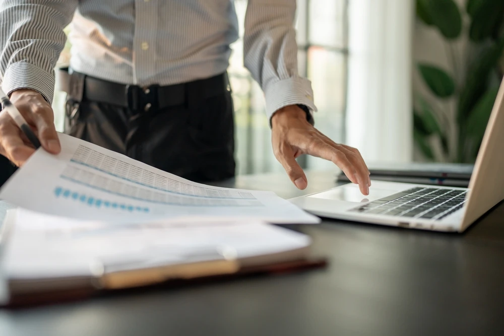 Une personne en chemise blanche signe un document officiel avec un stylo doré dans un environnement professionnel lumineux