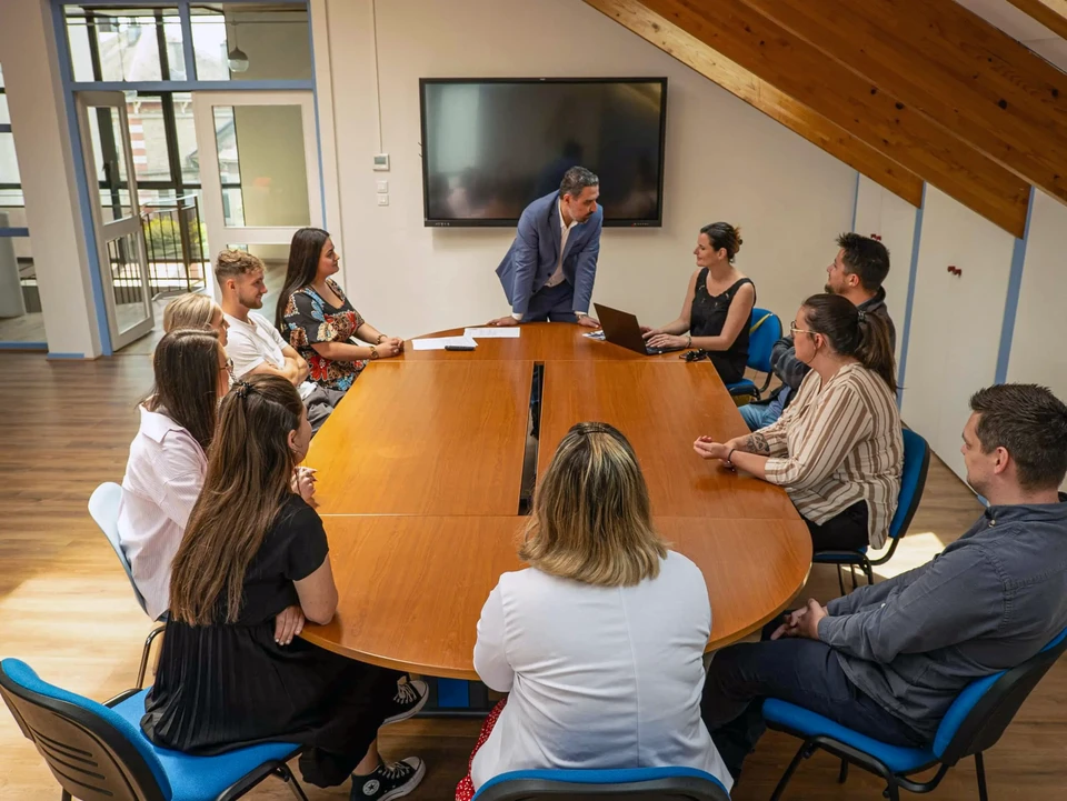 Homme d'affaires en costume sombre et cravate bleue pointant vers le mot "ACCOUNTING" lumineux, tenant une tablette dans l'autre main, arrière-plan flou de bureau moderne